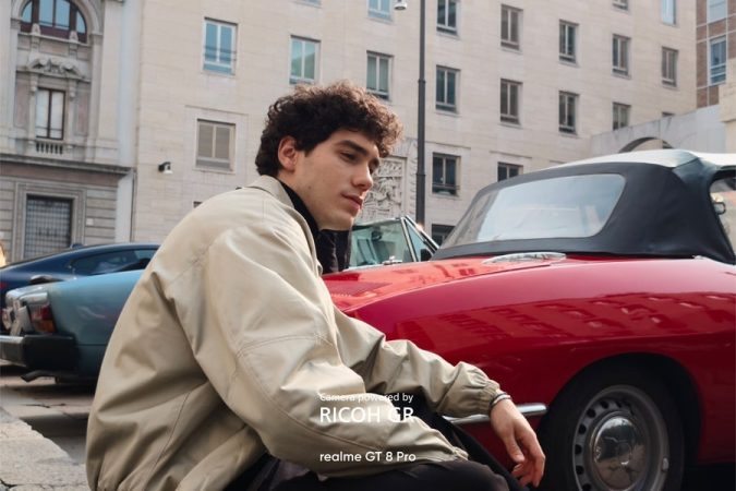 Portrait d'un jeune homme en blouson beige près d'une voiture de sport rouge, pris avec le realme GT 8 Pro