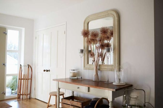 Un couloir d'entrée campagne chic avec une console ancienne patinée, un miroir à cadre doré vieilli et des fleurs séchées illustrant différents styles de décoration authentiques.
