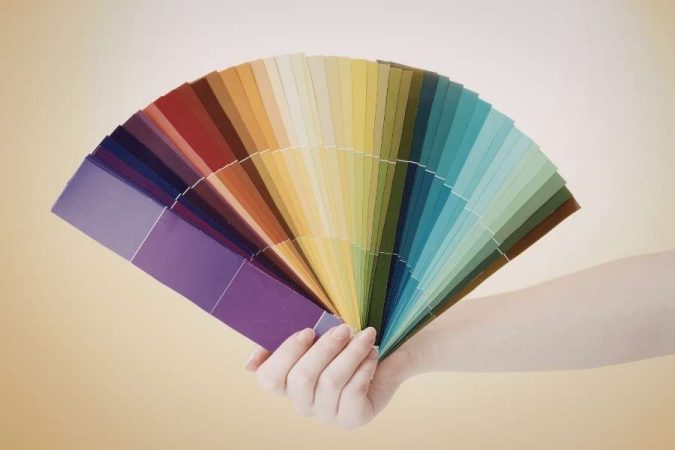 Un nuancier de peinture tenu à la main par une personne, s'ouvrant en éventail pour révéler une large gamme de couleurs.